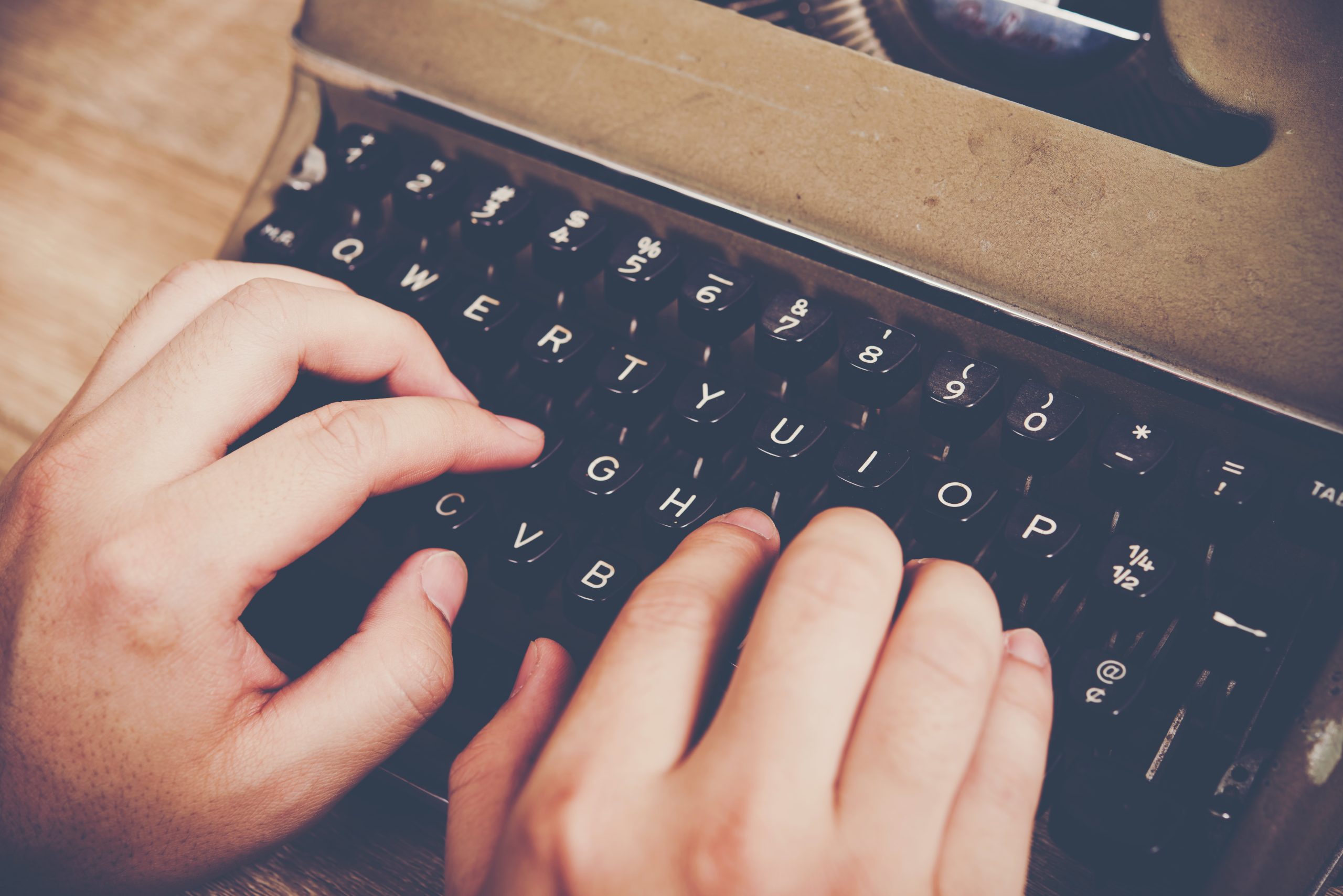 Hands typing on vintage typewriter on wooden table.